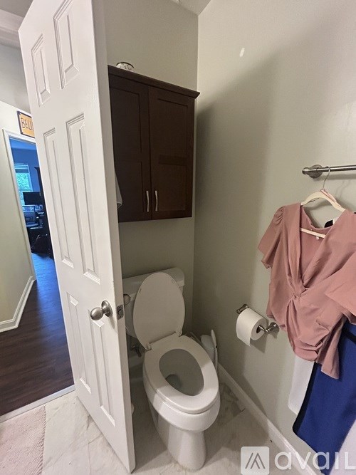 A toilet is in a small bathroom with a cabinet and a coat hanging on the wall.