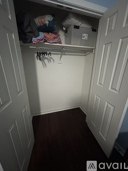 A small closet with a shelf and clothes hanging on a rack.