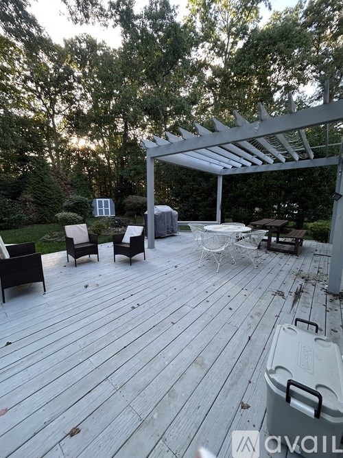 A wooden deck with a white pergola and chairs.