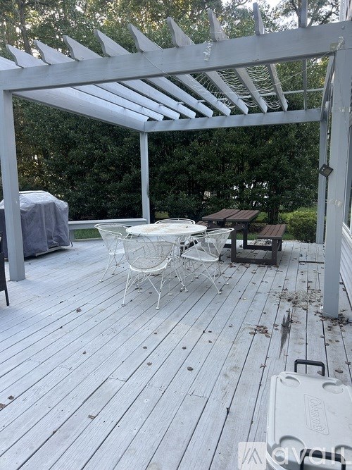 A white wooden deck with a table and chairs under a white pergola.