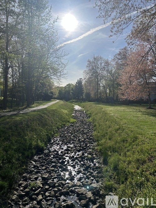 A stone path leads through a grassy field with trees on either side.