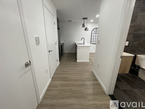 A hallway with a white door and a white kitchen area.