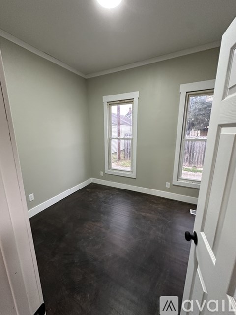 A room with a white door and a window with a view of a fence and trees.