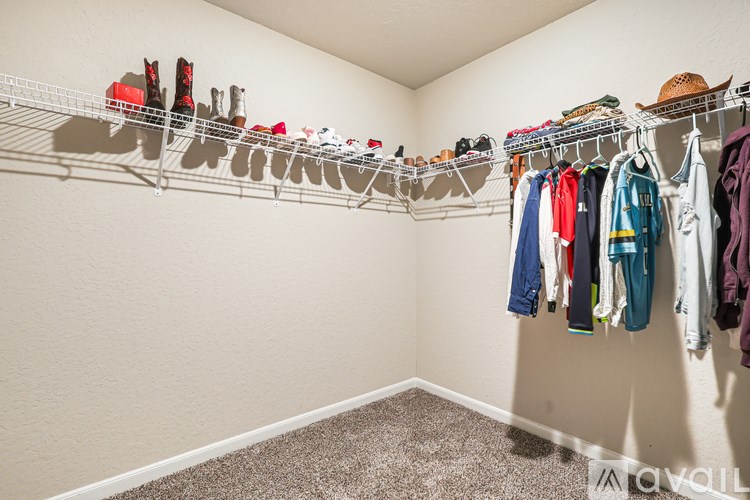 A room with a carpeted floor and a wall-mounted rack with clothes and shoes.