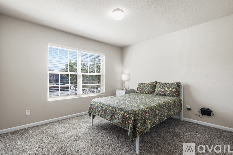 A bedroom with a floral bedspread and a window overlooking a street.