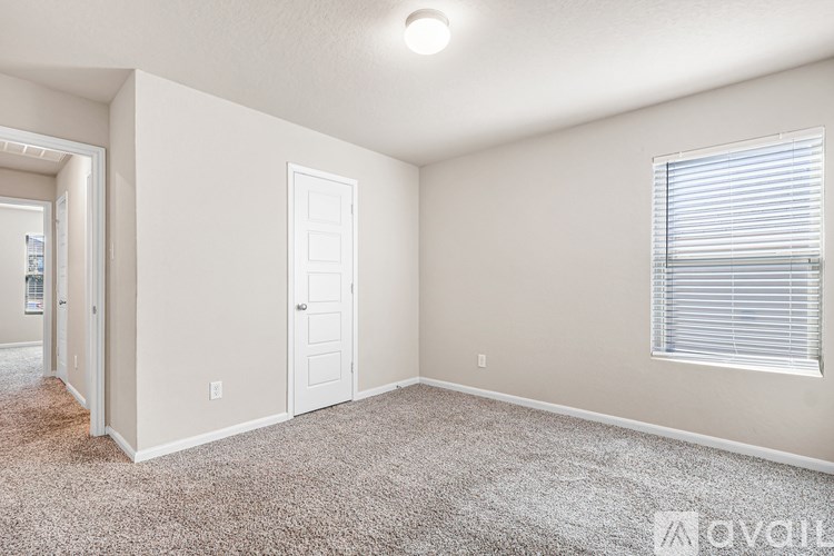 A room with a carpeted floor, a door, and a window with blinds.