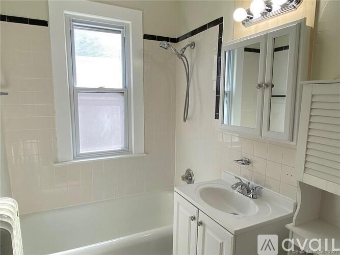 A white bathroom with a window, sink, and shower.