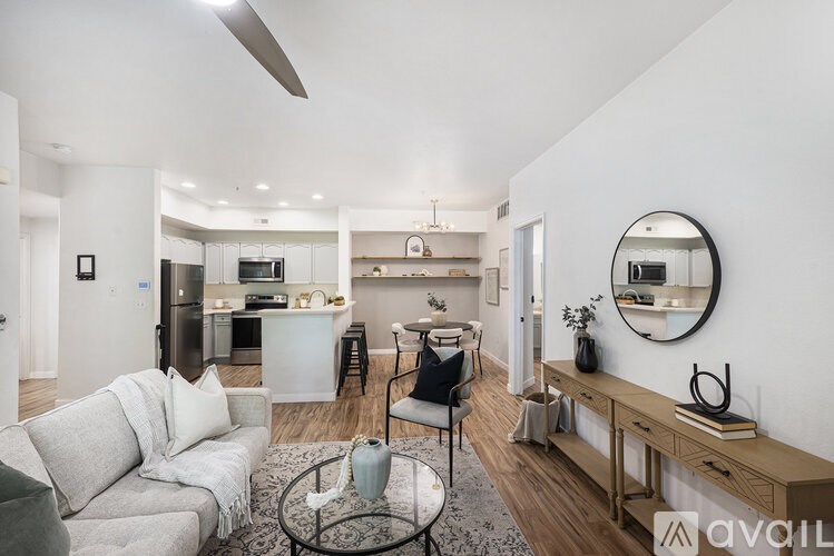 A modern living room with a grey sofa, a glass coffee table, and a round mirror on the wall.