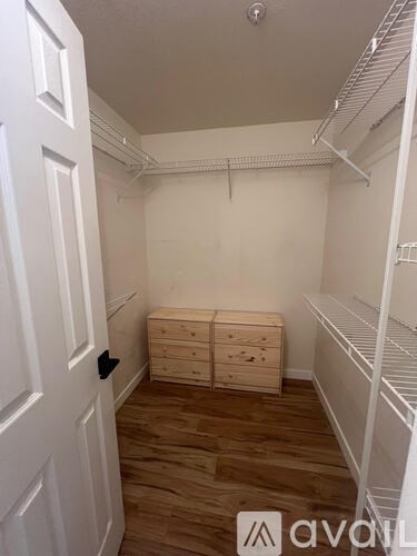 A white door opens to a room with a wooden floor and a white shelving unit.