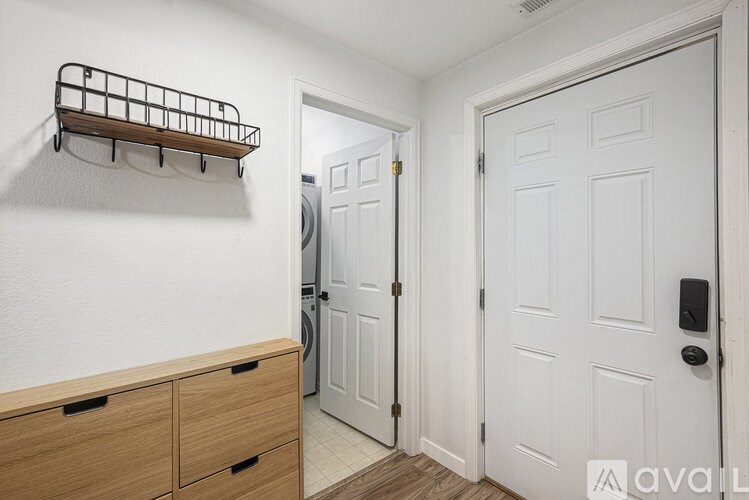 A white door is in a room with a white wall and a wooden shelf above it.