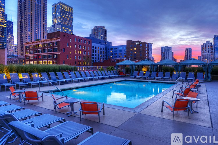 A rooftop pool with lounge chairs and a city skyline at dusk.