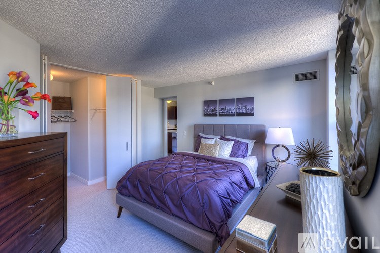 A bedroom with a purple bedspread and a wooden dresser.