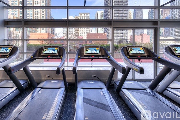 Three treadmills are lined up in a row with city buildings visible through the windows.