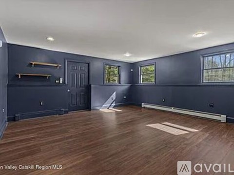 A spacious room with wooden flooring and a large window.