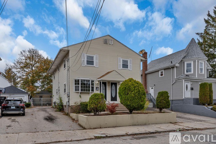 A house with a grey roof and a white door is surrounded by a small garden.