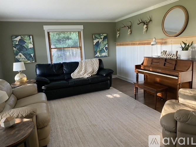 A living room with a black couch, a wooden piano, and a rug.