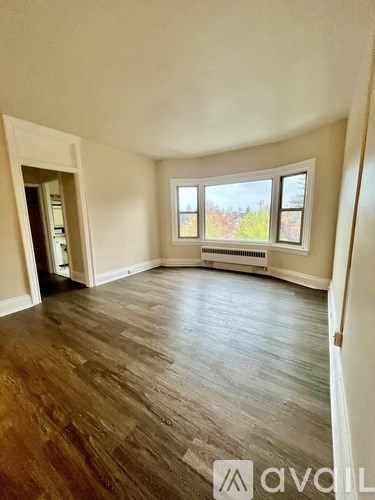 A room with wooden flooring and a window overlooking a tree-filled landscape.