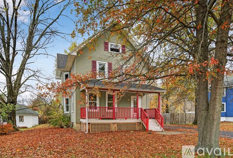 A house with a red porch surrounded by trees with orange leaves.