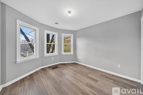 A room with a grey wall and a window showing trees outside.