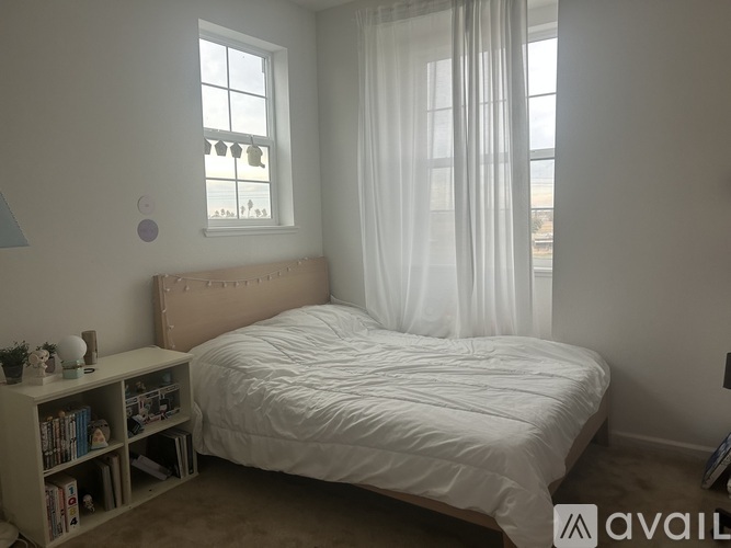 A bedroom with a large bed and a window with white curtains.