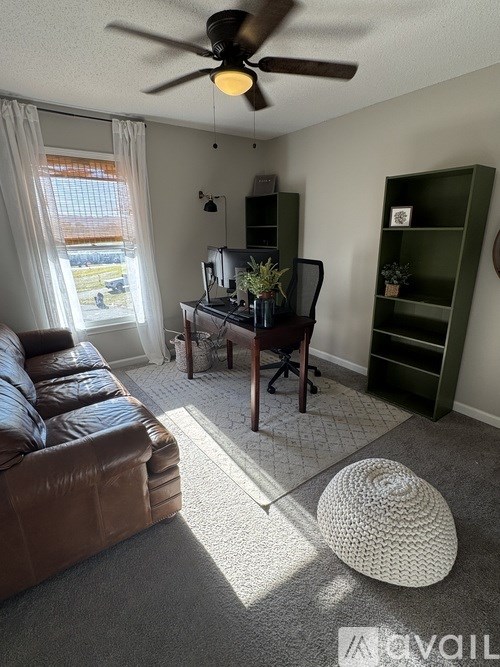 A living room with a brown leather couch, a ceiling fan, and a green bookshelf.