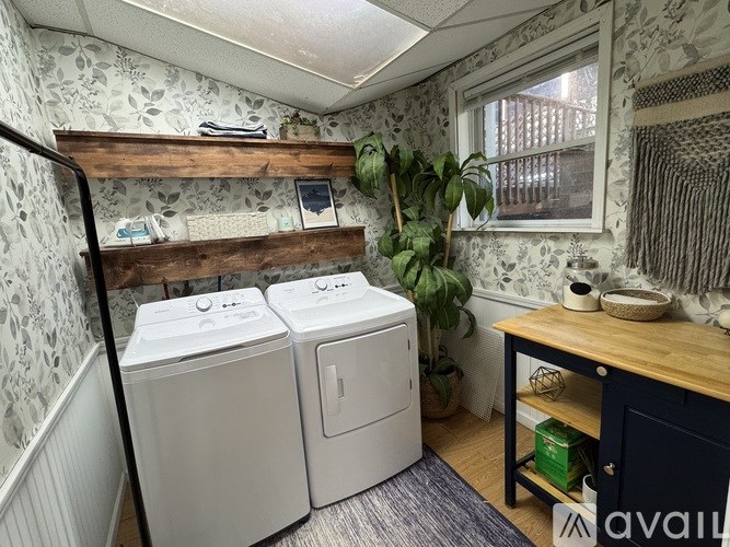 A laundry room with two washing machines and a wooden shelf above them.