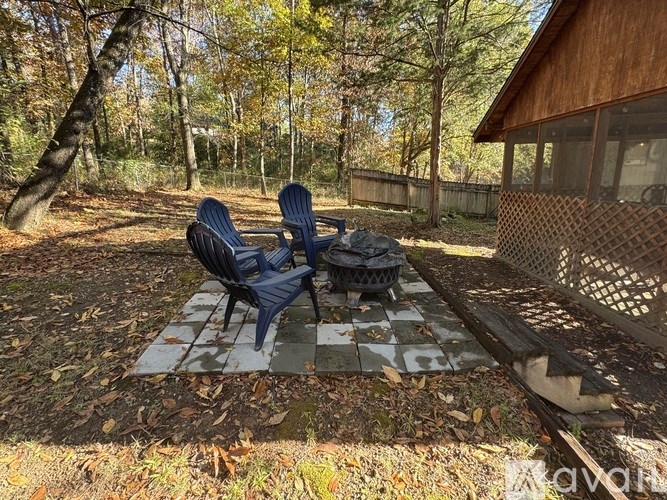 Two blue Adirondack chairs are on a checkered mat in a backyard.