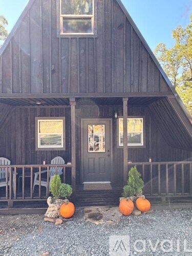 A wooden house with a black door and windows, decorated with pumpkins and a small tree.