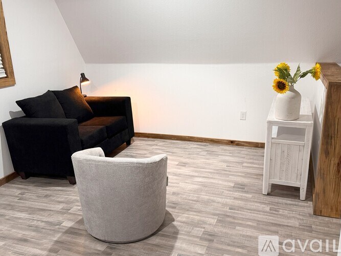 A living room with a black couch, a grey ottoman, and a white side table with sunflowers.