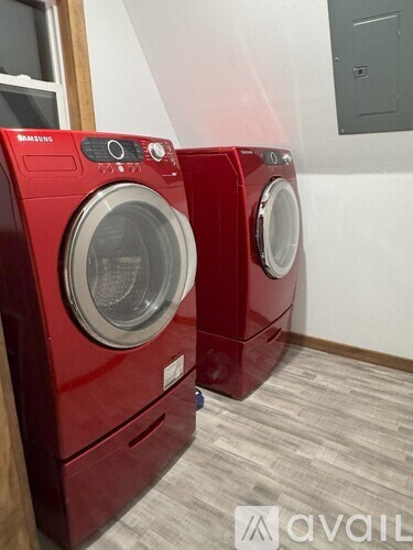 Two red Samsung front load washing machines in a laundry room.