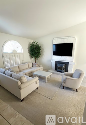 A living room with a white couch, a white chair, a white coffee table, a white fireplace, and a white television.