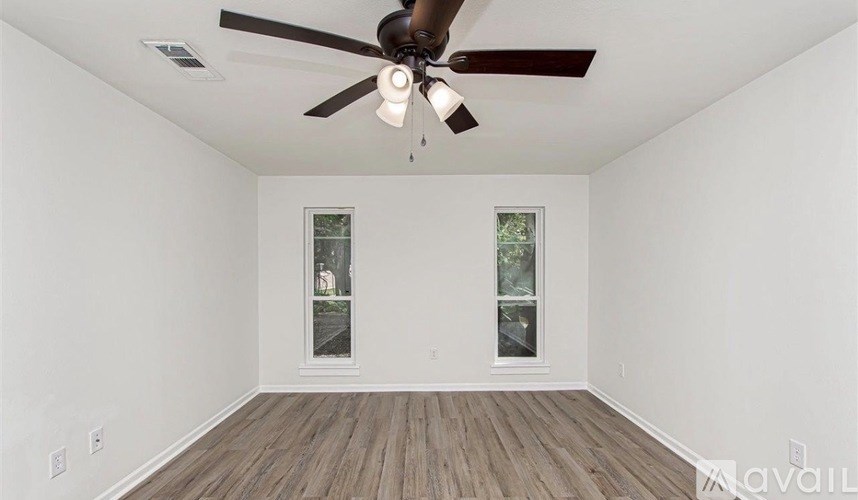 A room with a ceiling fan and two windows.