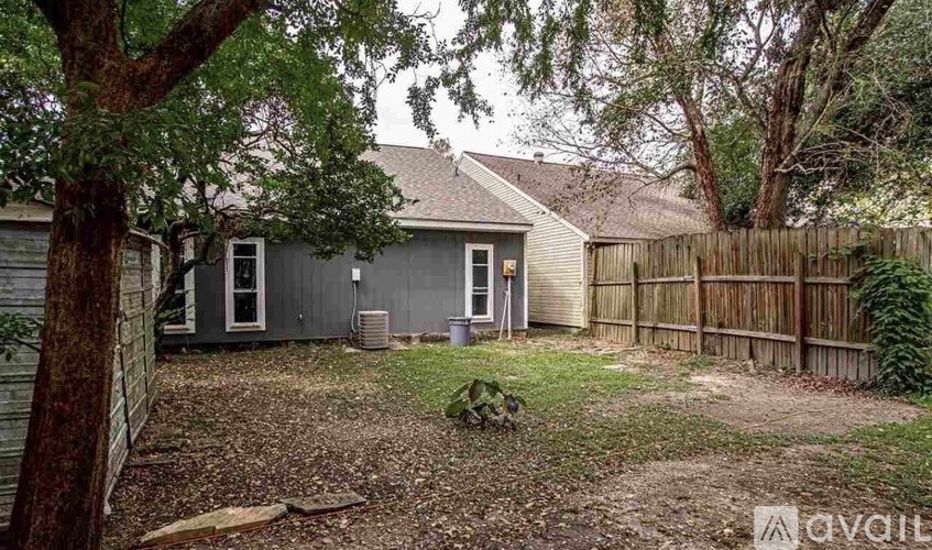 A grey house with a wooden fence and a tree in front.