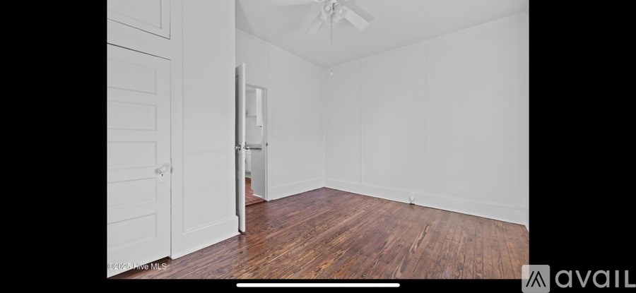 A room with wooden floors and white walls, with a door open to a hallway.