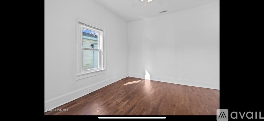 A room with wooden floors and white walls, with a window on the left side.