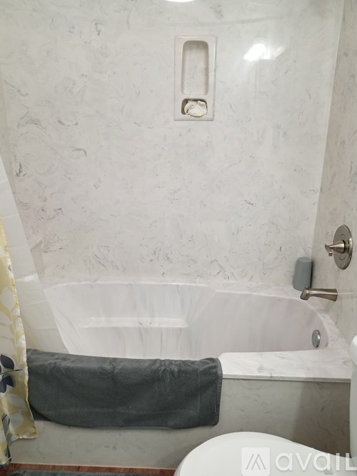 A bathroom with a white tub and grey towel.