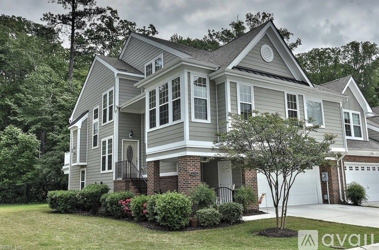 A house with a grey and white exterior is surrounded by greenery.