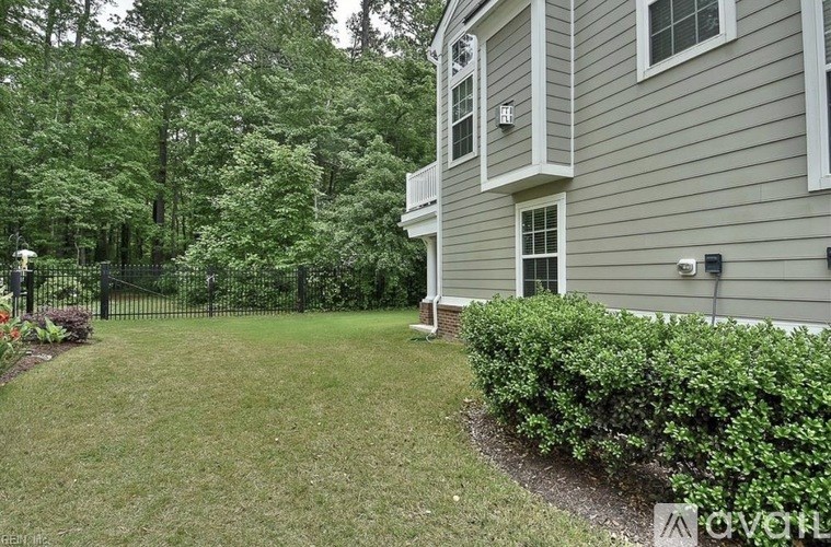 A house with a grey siding and a white window is surrounded by a green lawn and trees.