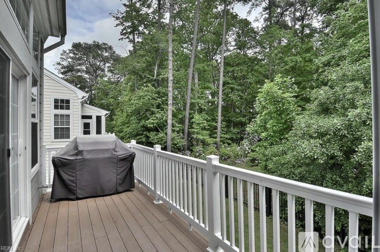 A white deck with a grey couch and trees in the background.