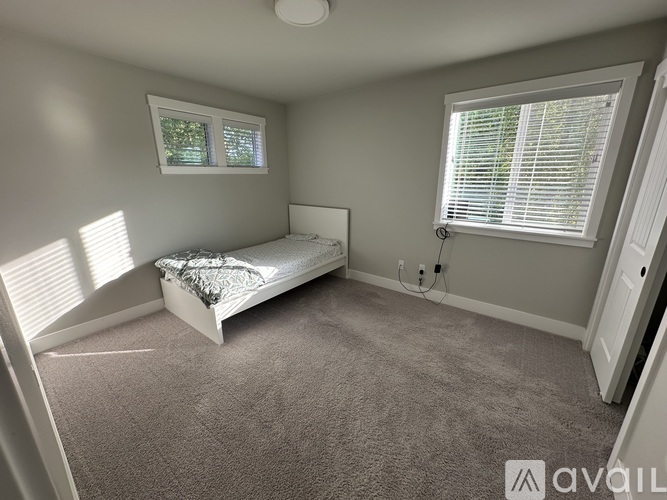 A bedroom with a bed, carpet, and two windows.