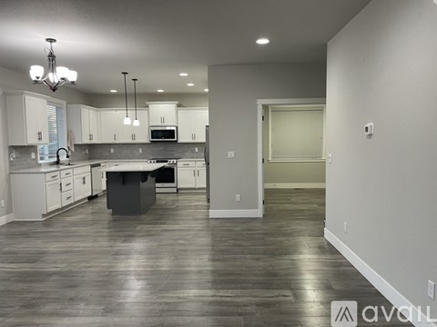 A spacious kitchen with white cabinets and a dark wood floor.