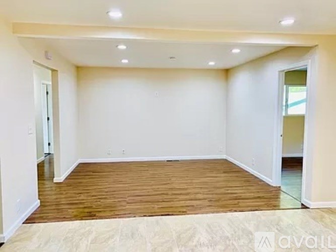 A spacious room with wooden flooring and white walls.