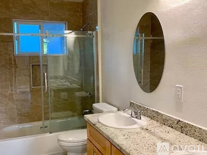 A bathroom with a round mirror, a sink, and a glass shower door.
