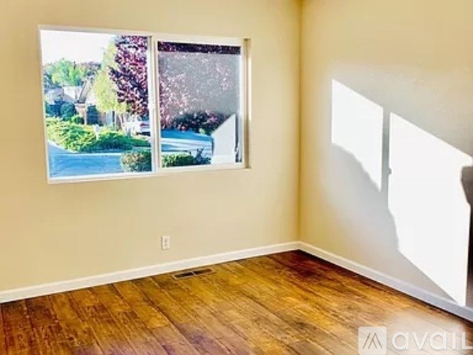 A room with wooden floors and a window showing a view of a street and trees.