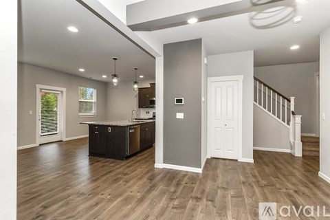A modern kitchen with wooden floors and a staircase in the background.