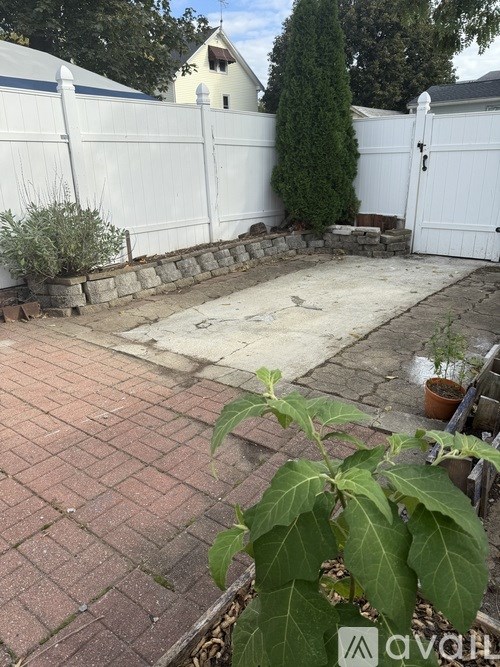 A backyard with a white fence and a brick patio.