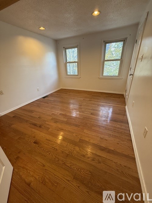 A room with wooden flooring and two windows.