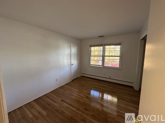 A room with wooden flooring and a window with a view of trees outside.