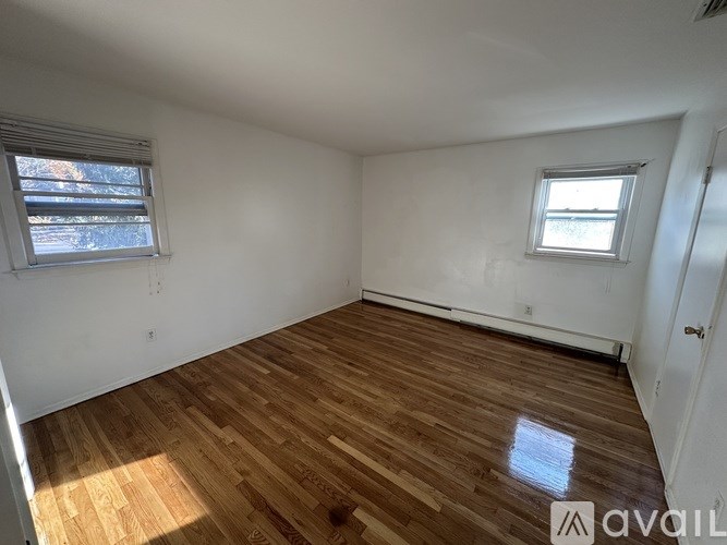 A room with wooden flooring and two windows.