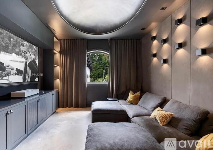 A modern living room with a grey sofa and a large screen on the wall.